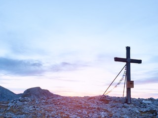 Praying flags fluttering  in the wind on the summit cross. Wooden crucifix on top of Alpine mountain