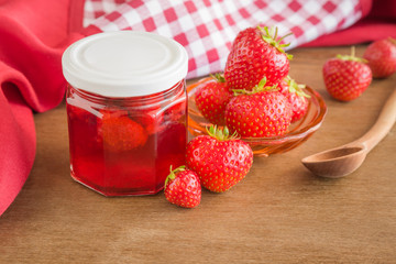Homemade strawberry jam in the glass jar. Red, fresh berries on the table in the kitchen. Tasty, sweet food preparation for wintertime.