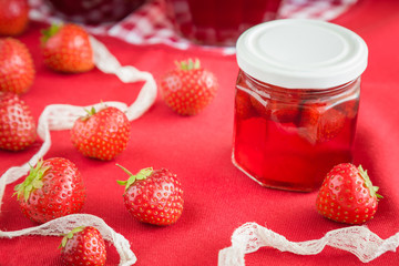 Homemade strawberry jam in the glass jar. Red, fresh berries on the table in the kitchen. Tasty, sweet food preparation for wintertime.