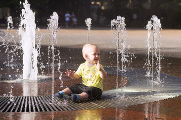 Cute toddler playing with water streams in fountain
