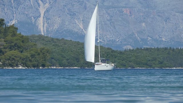 A sailboat gently basse the beautiful sunny sea shore of Greece islands.