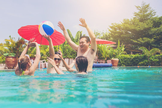 group of friends playing ball in outdoor swimming pool jumping into water on summer vacation.