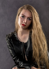 beautiful young woman in a leather jacket posing on a gray background