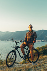 Handsome Young Man Standing With Bike On Coast And Enjoying View of Nature Sunset Vacation Traveling Relaxation Resting Concept