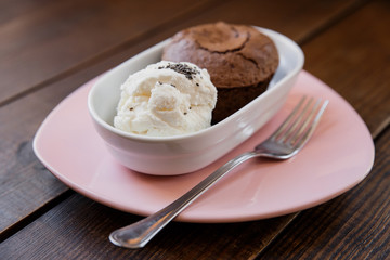 Chocolate lava cake with ice cream covered with poppy seeds, in a white bowl, on a pink plate, fork near by. Wooden table. Selective focus, small depth of field. 
