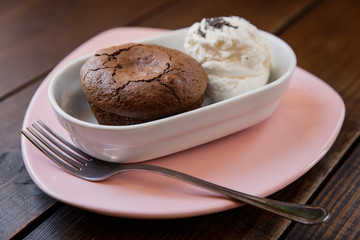 Chocolate lava cake with ice cream covered with poppy seeds, in a white bowl, on a pink plate, fork near by. Wooden table. Selective focus, small depth of field. 