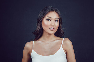 Portrait of a beautiful asian woman with makeup and light curls on black background.