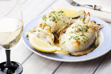Cuttlefish With garlic, parsley and lemon next to a glass of wine, fork and napkin. Food..