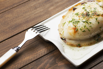Cuttlefish with garlic and parsley and lemon next to fork on wooden table.