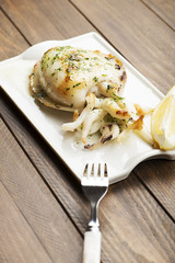 Cuttlefish with garlic and parsley and lemon next to fork on wooden table. Vertical studio shot.