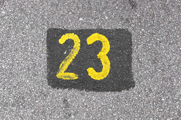 Yellow imprint of the number twenty three on an asphalt street.