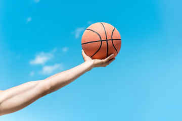 cropped shot of hand holding basketball ball against clear blue sky