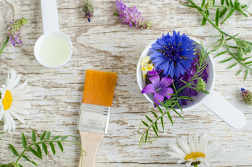 Obraz na płótnie Canvas Plastic scoop with various field flowers and cosmetic brush. Ingredients of natural cosmetic. Organic skincare, homemade cosmetics and spa concept.