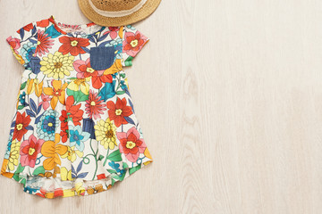 Colorful floral baby dress and straw hat on a light gray wood background. Baby girl summer fashion accessories. Top view, copy space