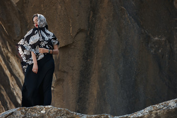 Beautiful young oriental woman in a long black dress and oriental Shawl in the mountains on a cliff.