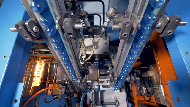 PET bottle preforms grabbed and elevated to enter blowing chamber. 