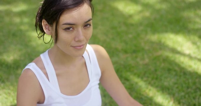 Serene young woman meditating on a green lawn with her eyes closed and smile of bliss