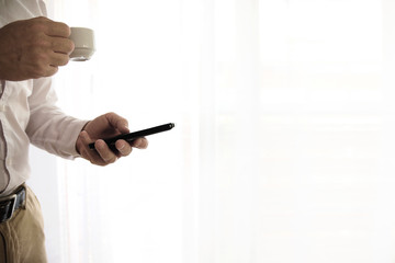 Adult man holding a cup of coffee while using a mobile. Empty copy space for Editor's text.