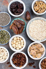 Ingredients for homemade granola, oats, different nuts and raisins, dates, seed on the grey stone background, top view