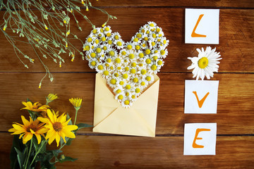 Heart with chamomile flowers on a wooden background