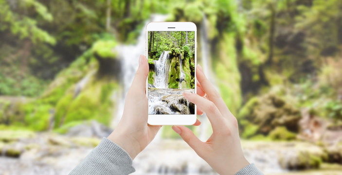 Girl taking photo of waterfall with smartphone in the woods