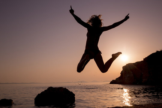 Happy young woman jumping on the beach at sunset