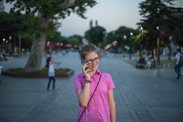 A young girl standing on the street, in the park, using a mobile phone, a story, a smile on her face, modern technology