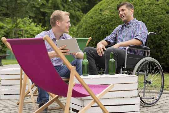 Positive man on wheelchair drinking with friend