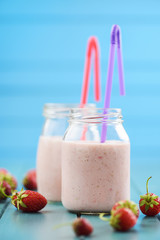 Healthy milk cocktail with fresh strawberries in mason jars on blue background