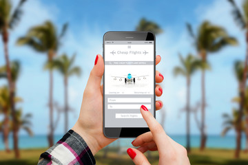 Person using cheap flights app on phone, palm trees and beach in background