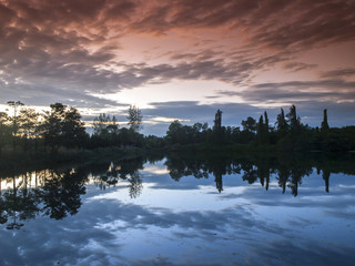 Fototapeta premium The setting sun and clouds reflect in a lake in east Thailand (filtered).