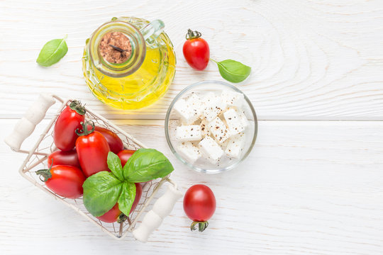 Salad ingredients. Cherry tomatoes, basil, feta cheese and olive oil on white wooden background, top view, copy space