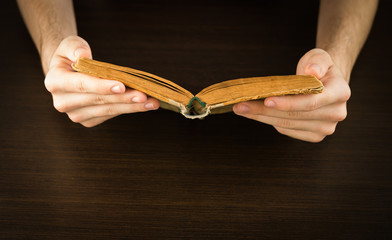 Hands of an young man holding a old book