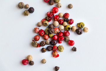 Different types of peppercorns - black, white, pink and green pepe verde - on white. Top view. Copy space.