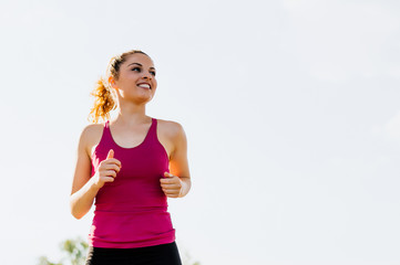 Portrait of attractive blonde female runner running in city park