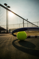 Tennis ball and racket on hard court under sunlight