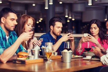 friends with smartphones dining at restaurant