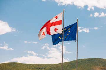The European Union and Georgian flags fly beside each other, on a background mountain and sky .