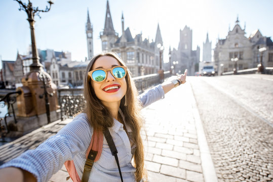 Young woman tourist making selfie photo standing on the bridge with beautiful view on Gent city in Belgium