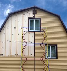 Beige siding panels mounting with scaffolding on beautiful rural house in sunny day front view