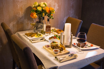 Served table with dishes from meat, chicken and fish with wine and whiskey. Romantic dinner in the restaurant by candlelight