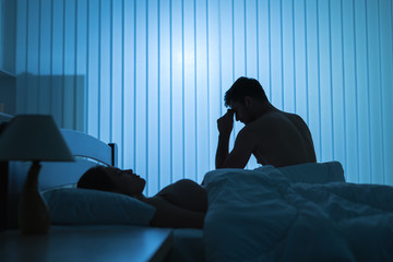 The worried man sit near near sleeping woman in the bed. night time