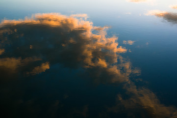 Naklejka na ściany i meble Reflection on the surface of calm water - orange clouds and blue sky during sunset