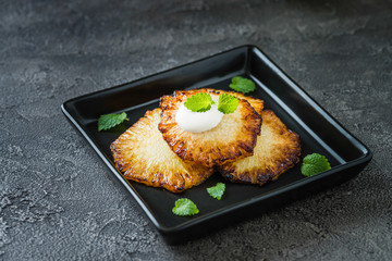 Fried pineapple slices with creme fraiche, dark background