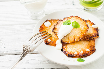 Fried pineapple slices with creme fraiche, white wooden table