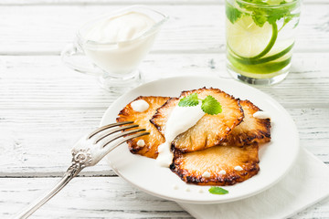 Fried pineapple slices with creme fraiche, white wooden table
