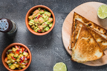 Grilled quesadillas (tortillas) with salsa, guacamole. Dark background, top view.