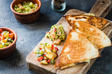 Grilled quesadillas (tortillas) with salsa, guacamole. Dark background.