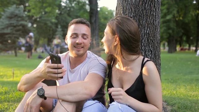 Guy and girl listening to music on the phone in a park under a tree
