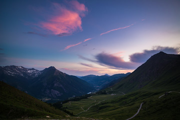 Dirt mountain road leading to high mountain pass in Italy (Colle delle Finestre). Expasive view at sunset, colorful dramatic sky, adventures in summer time, Italian Alps.